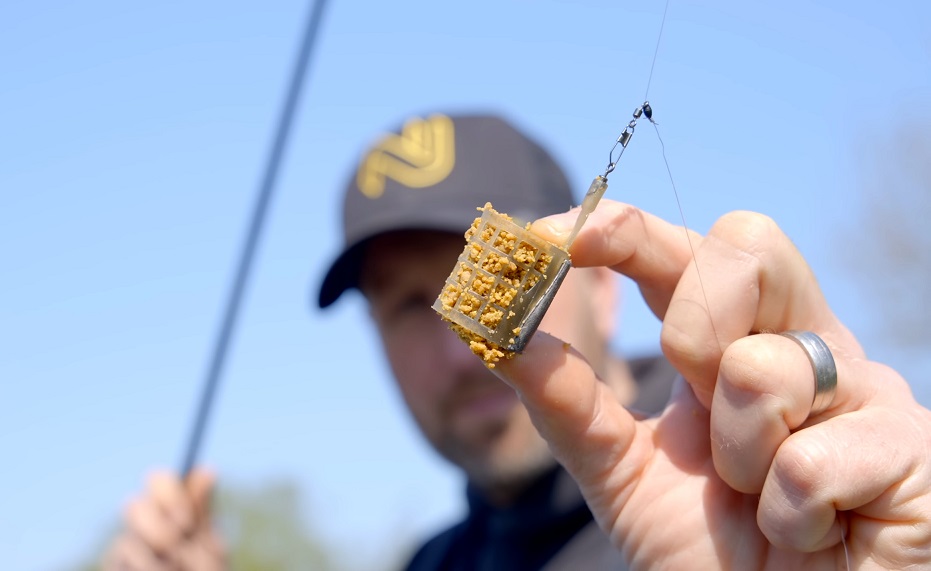 A man is holding a method feeder in his hand